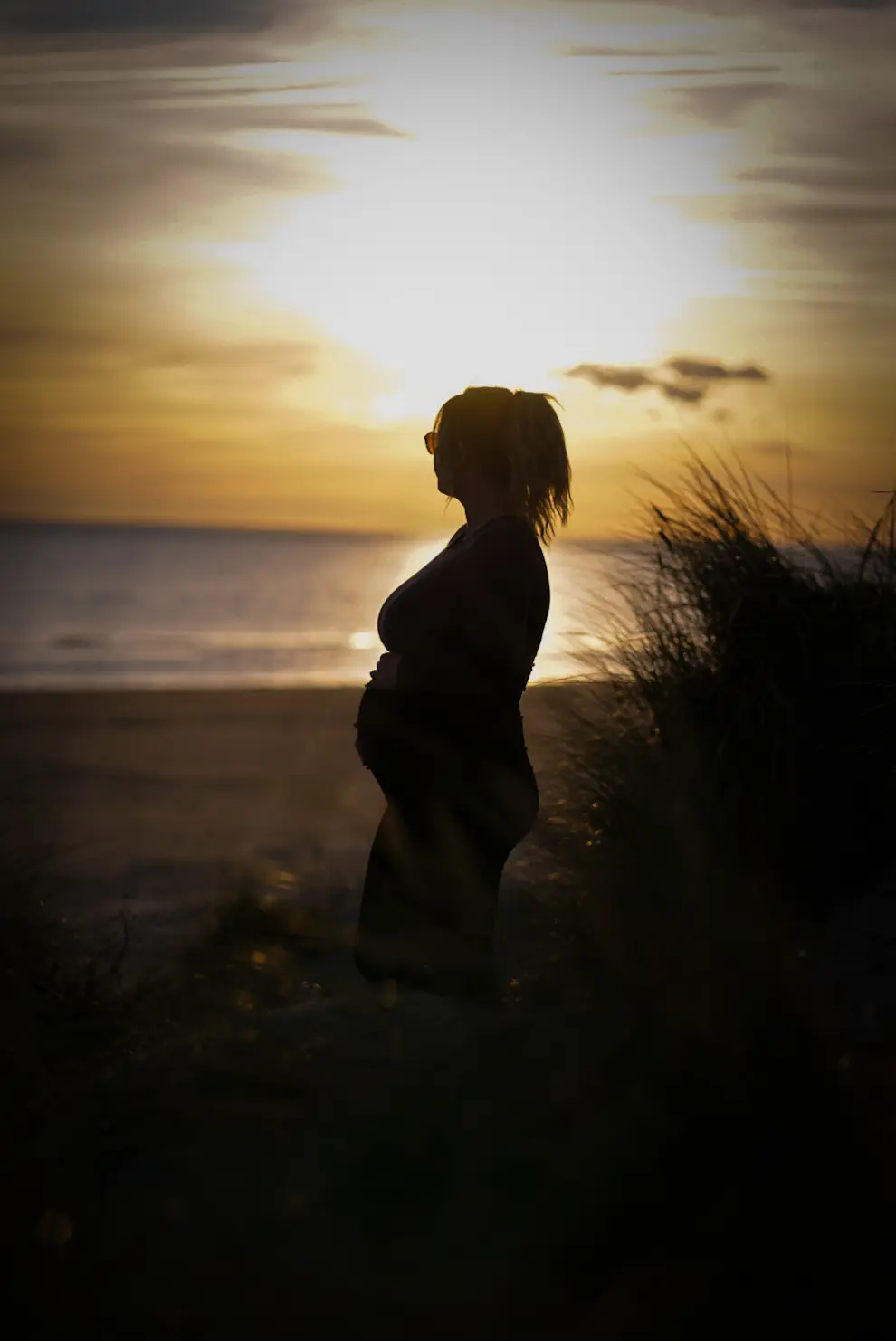 Babybauch-Silhouette zwischen Dünen und Meer