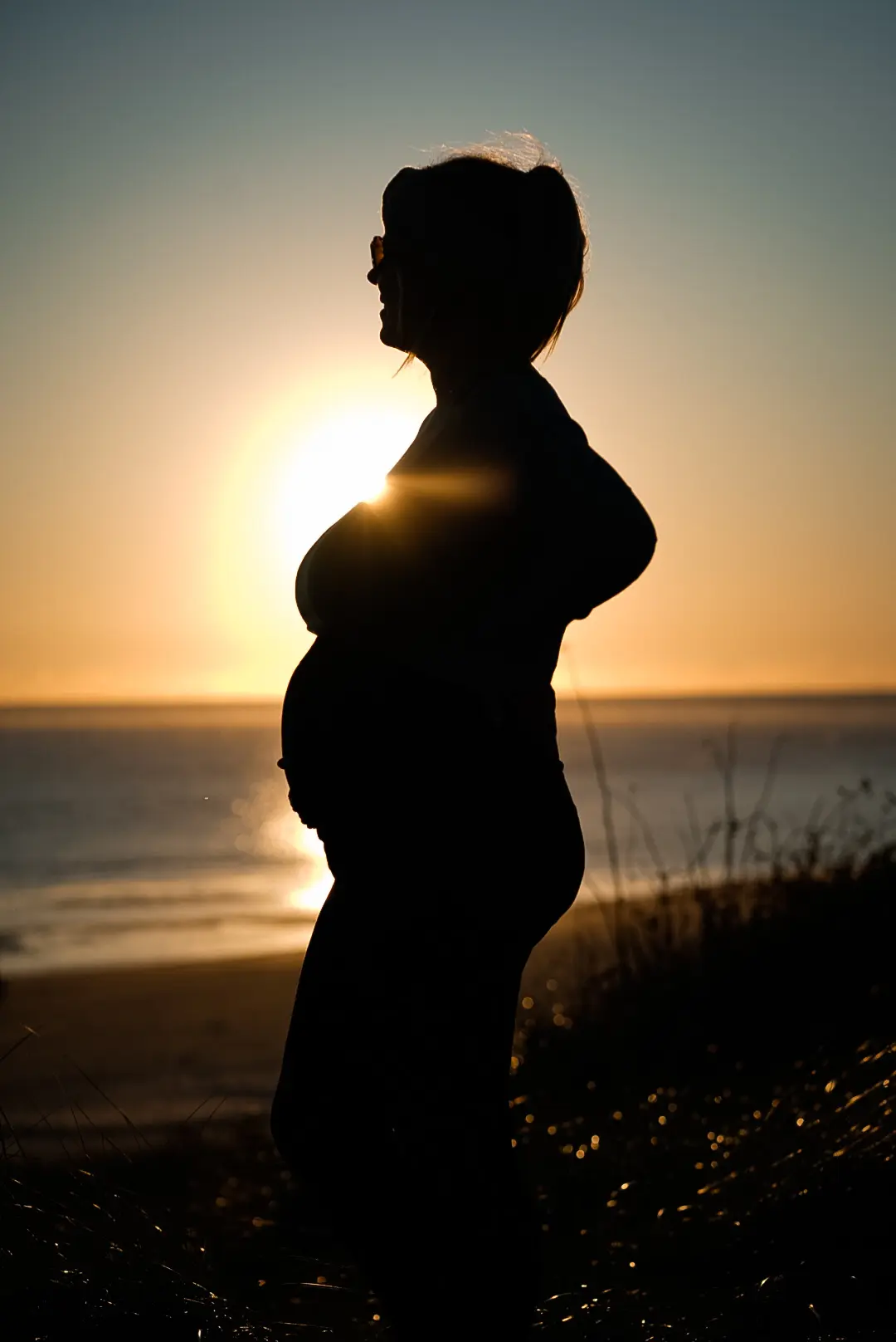 Babybauch-Portrait mit goldenem Gegenlicht am Meer