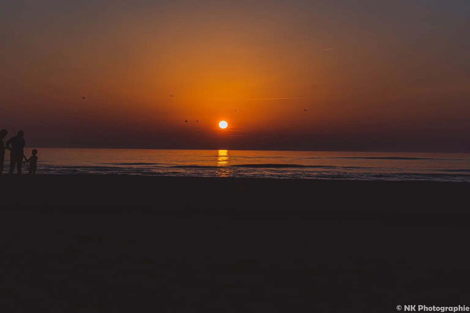 Goldener Sonnenuntergang am Meer mit einer Familie am Strand